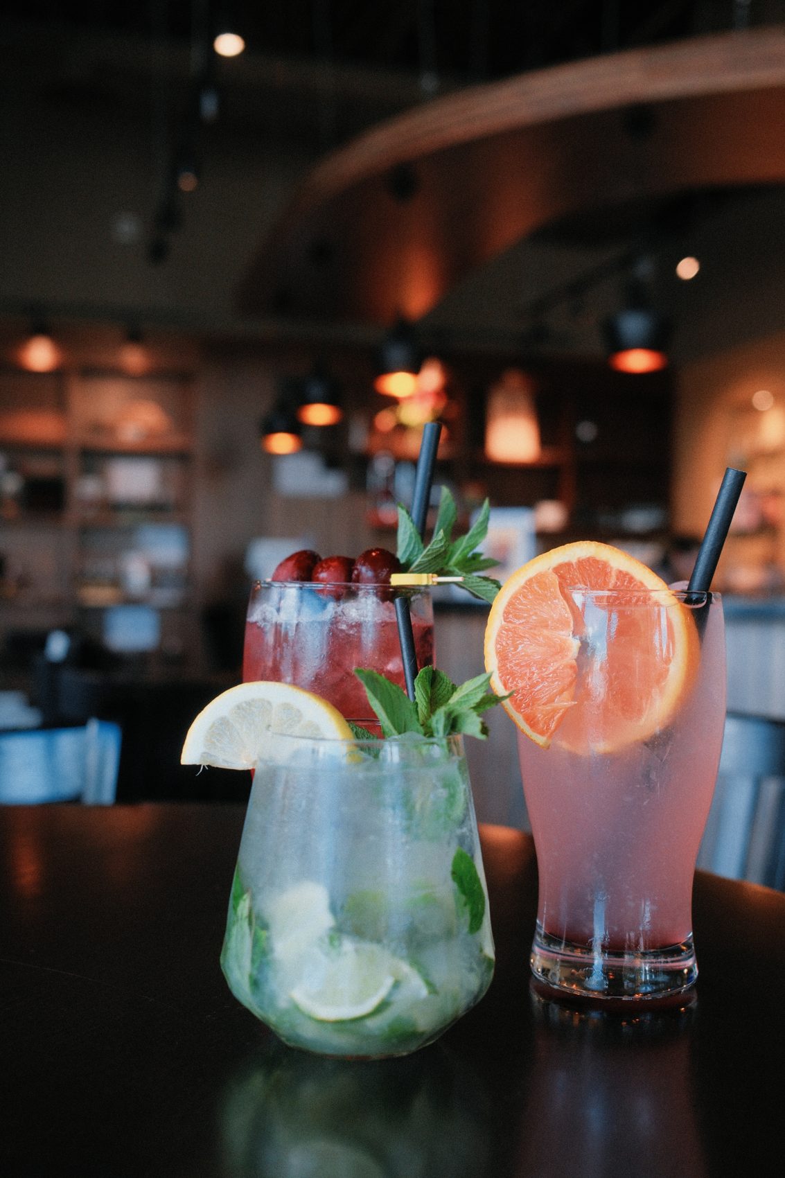 Cocktails garnished with citrus and mint on a dark bar